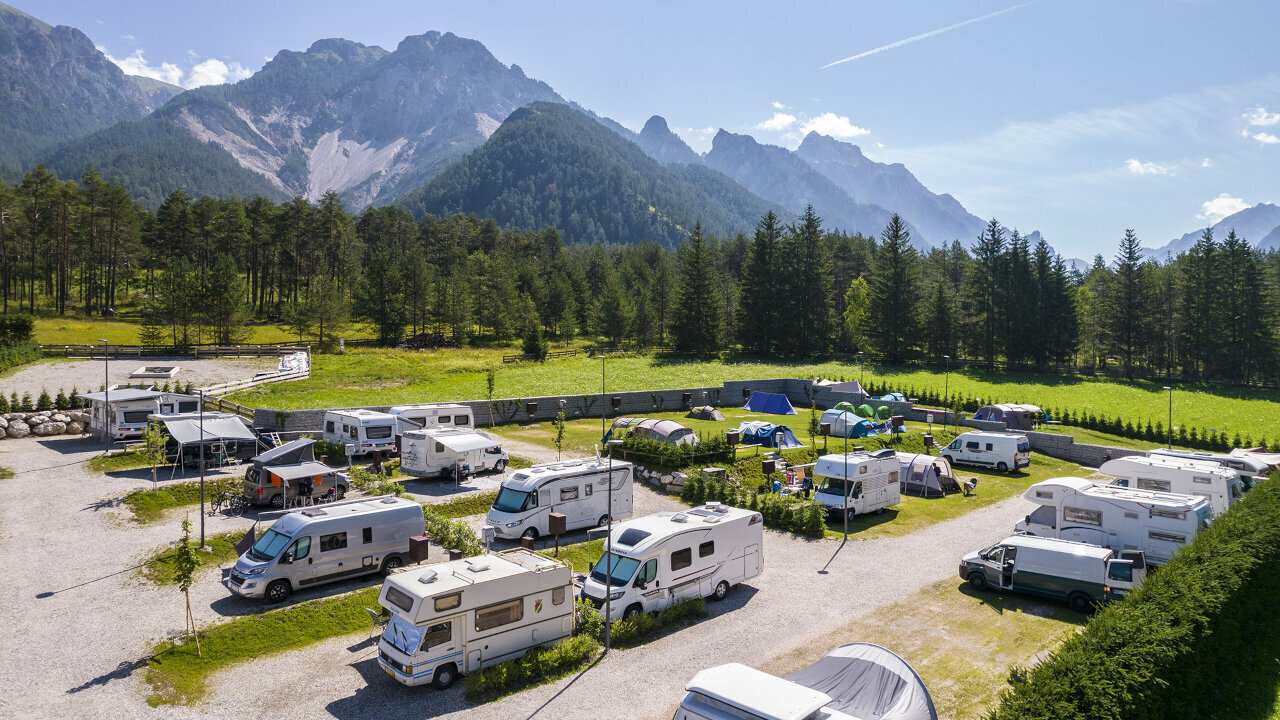 Campground with RVs and tents surrounded by trees and mountains under a clear blue sky. - Camping Al Plan