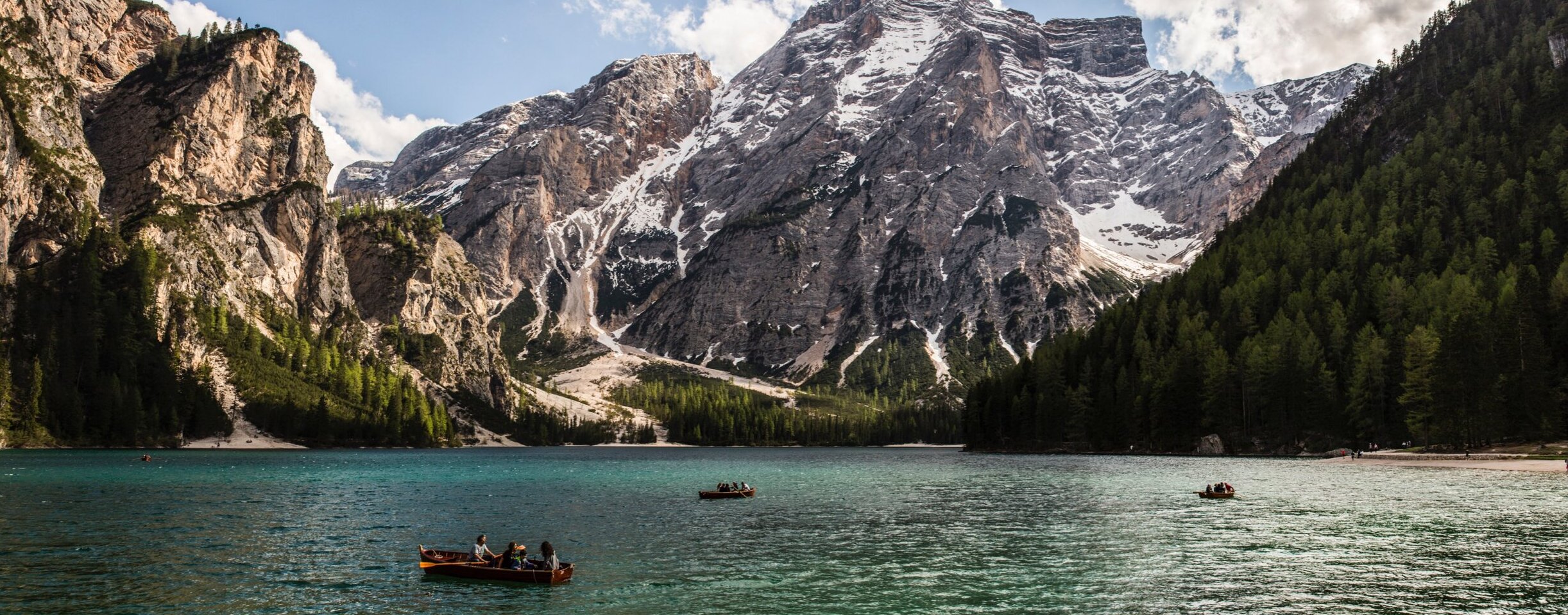 Schneebedeckte Berge, Wälder und Boote auf einem türkisfarbenen See unter einem teilweise bewölkten Himmel. - Camping Al Plan