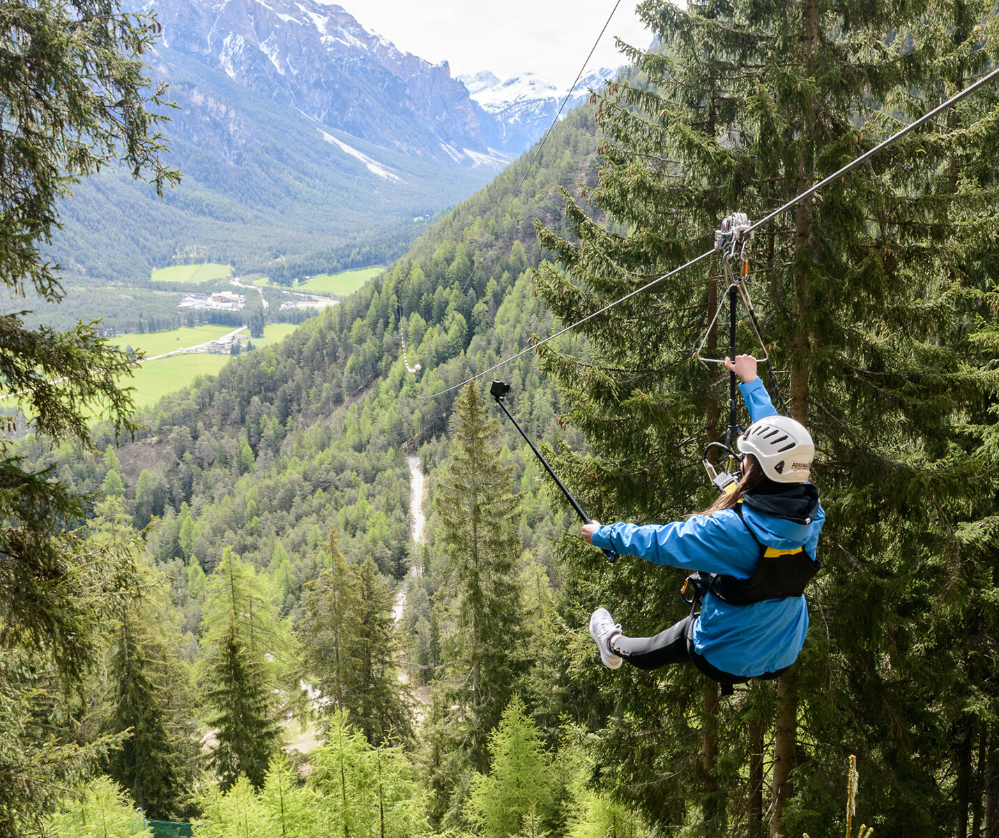 Eine Person, die mit einem Selfie-Stick durch ein bewaldetes Berggebiet gleitet, mit Blick auf ein malerisches Tal darunter. - Camping Al Plan