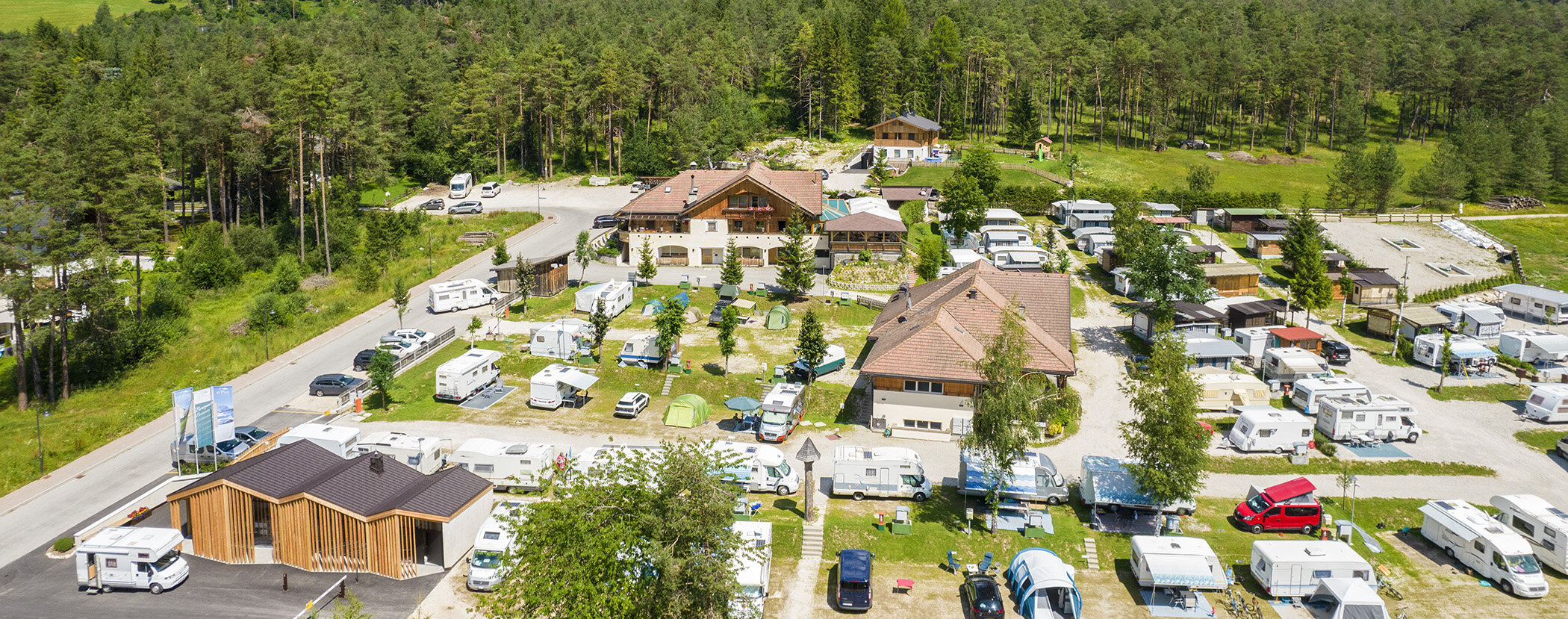 Aerial view of a campground with many RVs, buildings, and trees in a rural area. - Camping Al Plan