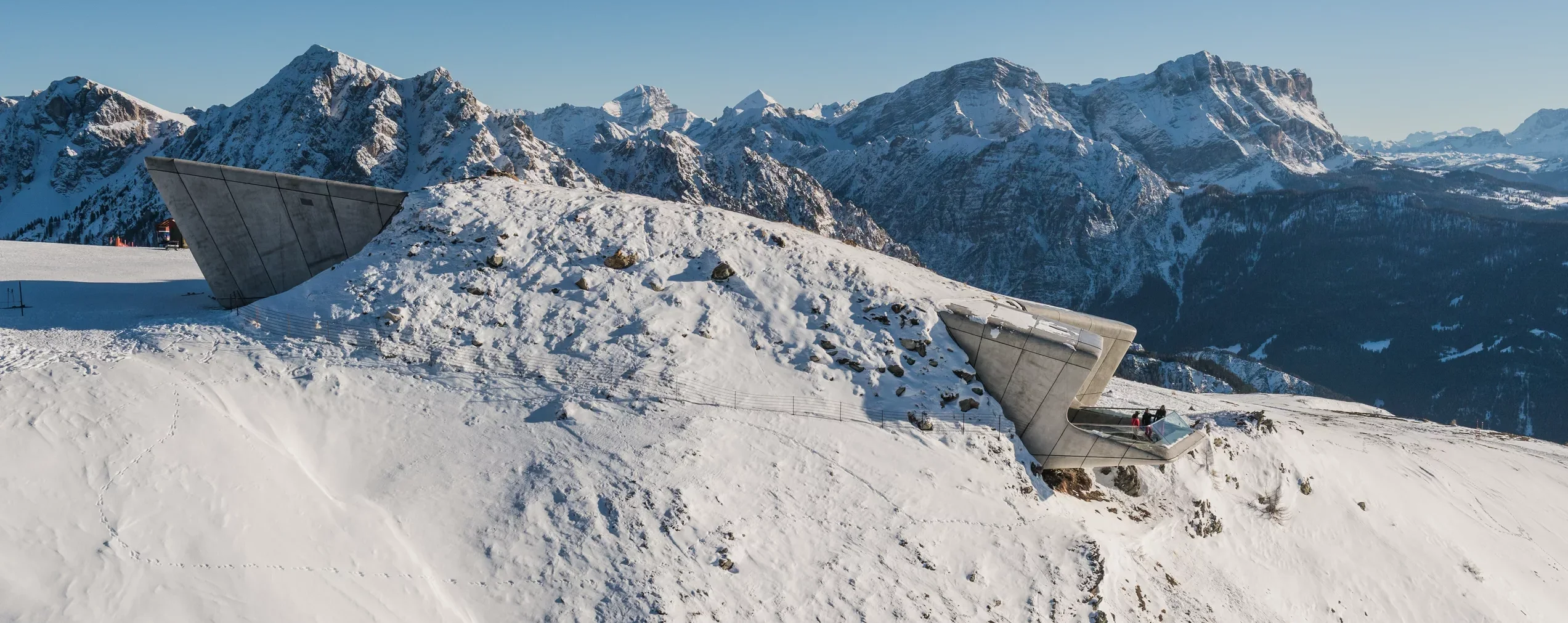 Betonbauten auf einem verschneiten Bergkamm mit schroffen, schneebedeckten Gipfeln im Hintergrund. - Camping Al Plan